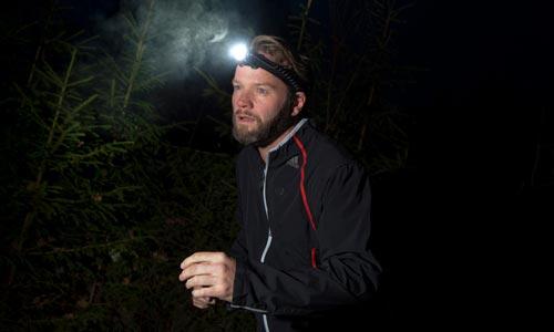 En man springer med en pannlampa i en mörk skog