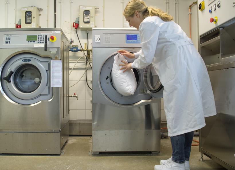 Kvinna stoppar in en kudde i en tvättmaskin.